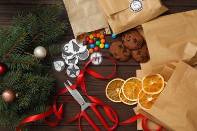 Photo of Flat lay composition with gift bags, treats and Christmas decor on wooden table. Creating advent calendar