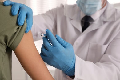 Doctor vaccinating young woman against Covid-19 in clinic, closeup