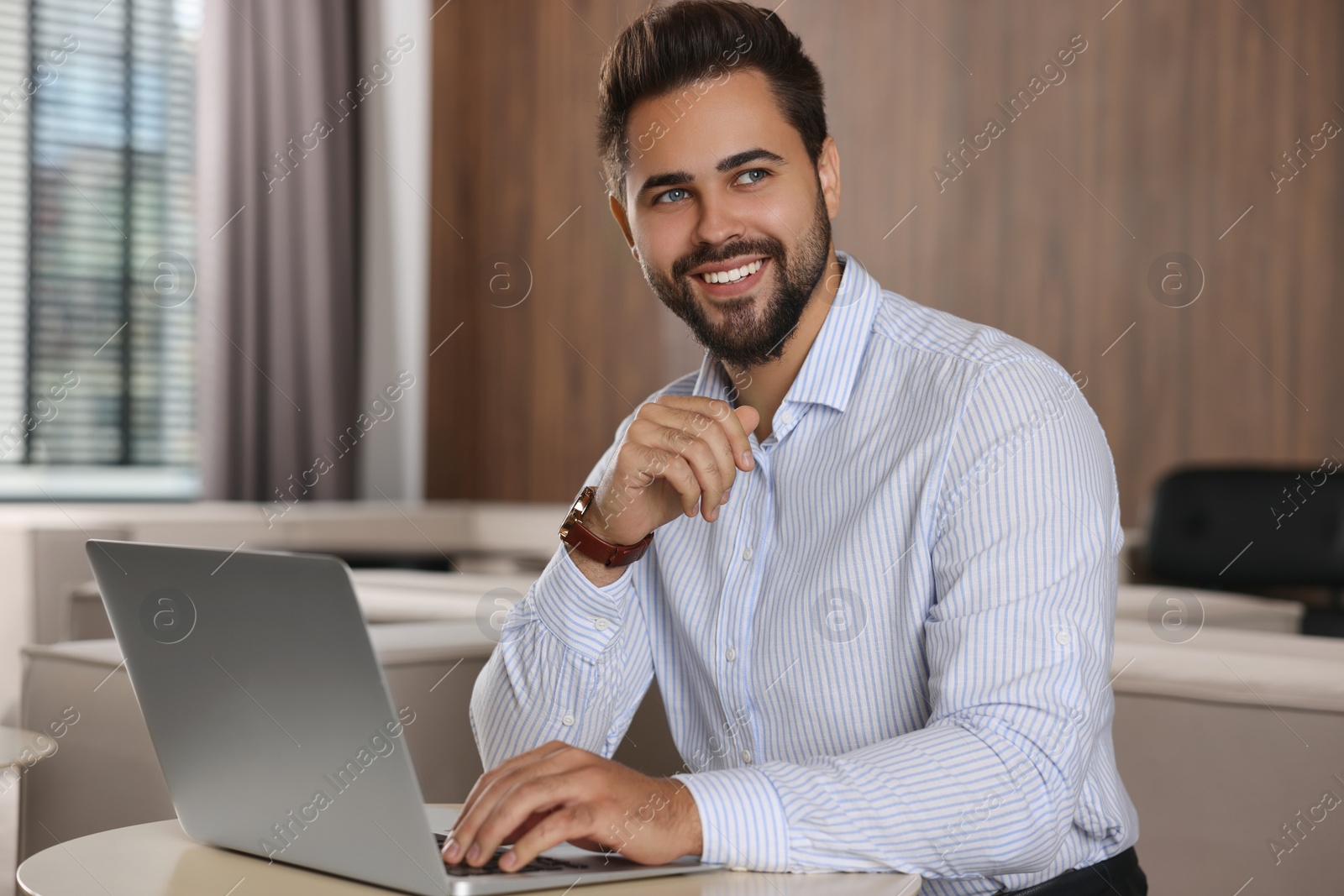 Photo of Happy young man working on laptop at table in office