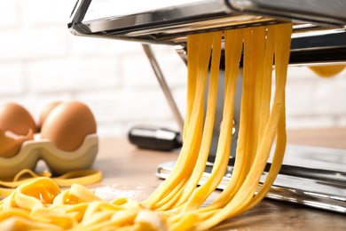 Photo of Pasta maker machine with dough on wooden table, closeup
