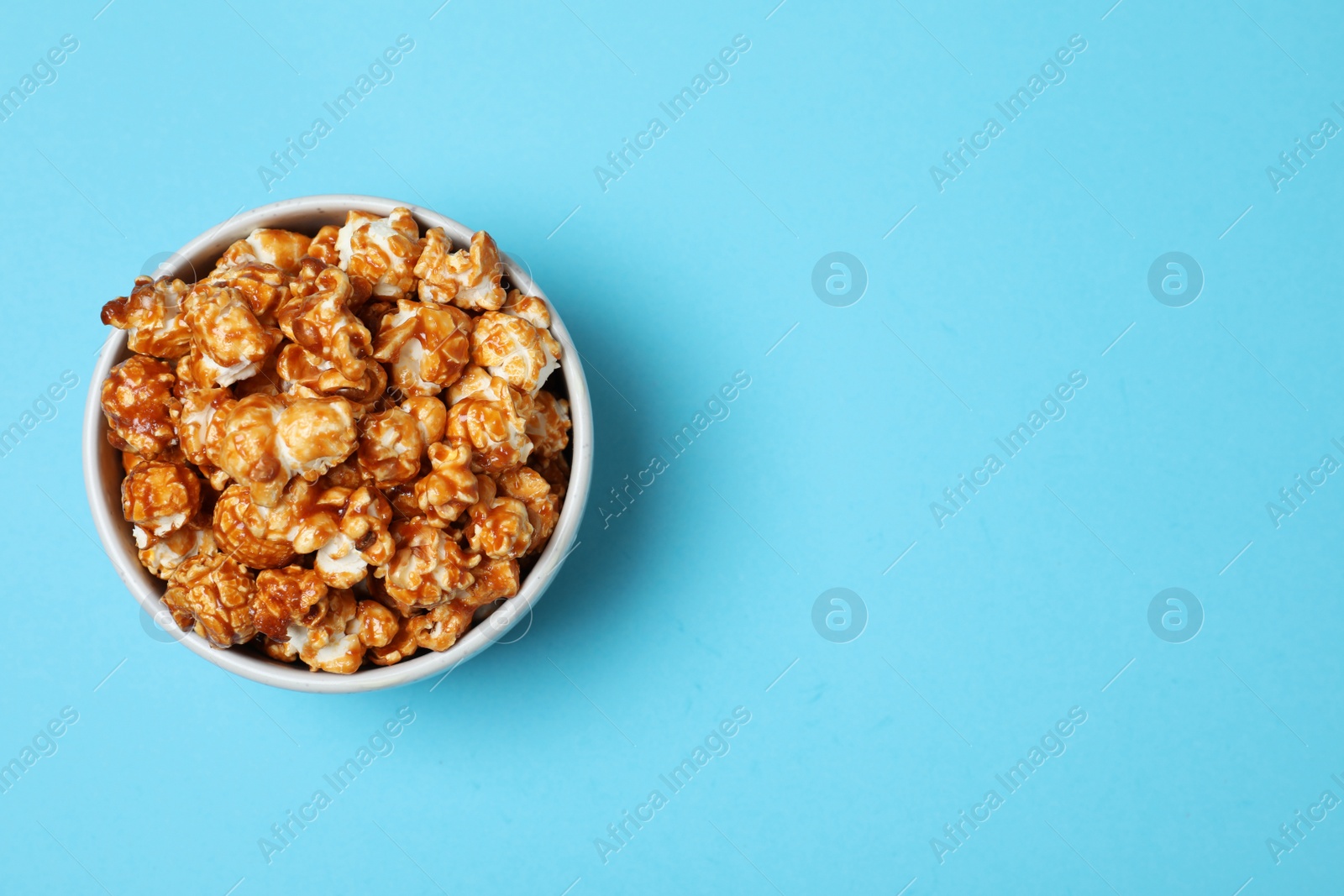 Photo of Bowl with caramel popcorn and space for text on color background, top view