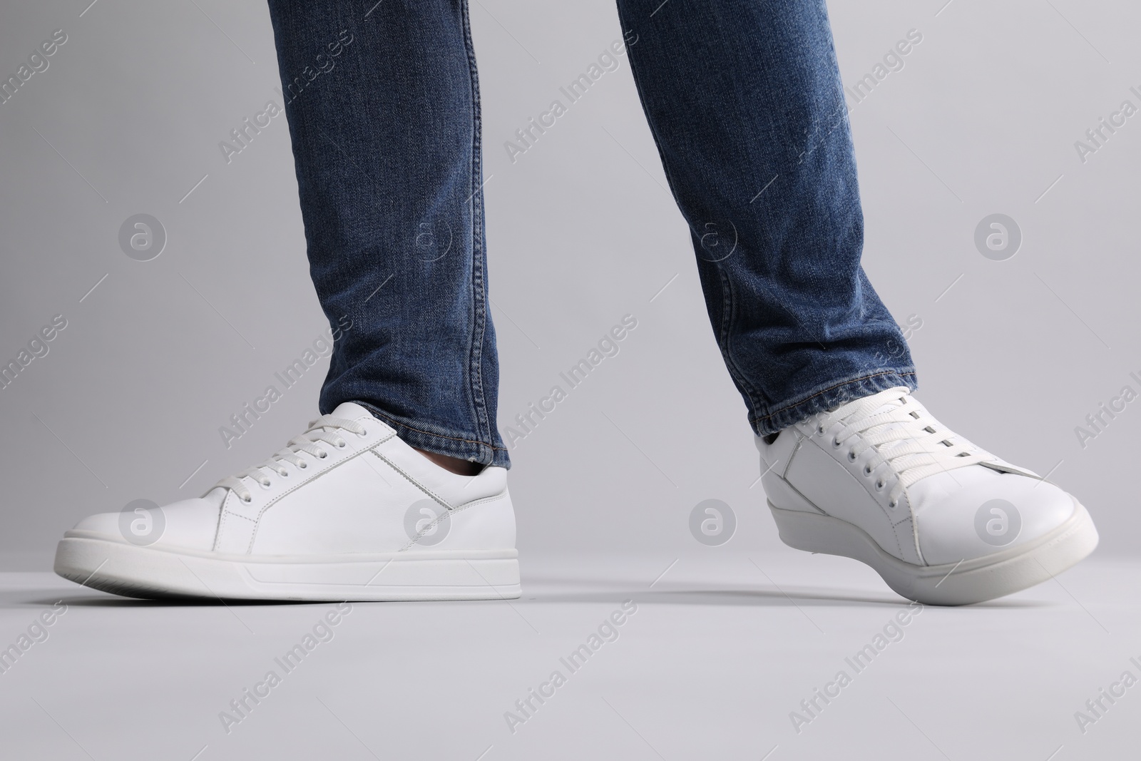 Photo of Man wearing stylish white sneakers on grey background, closeup