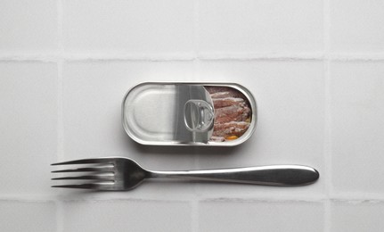 Canned anchovy fillets and fork on while tiled table, top view