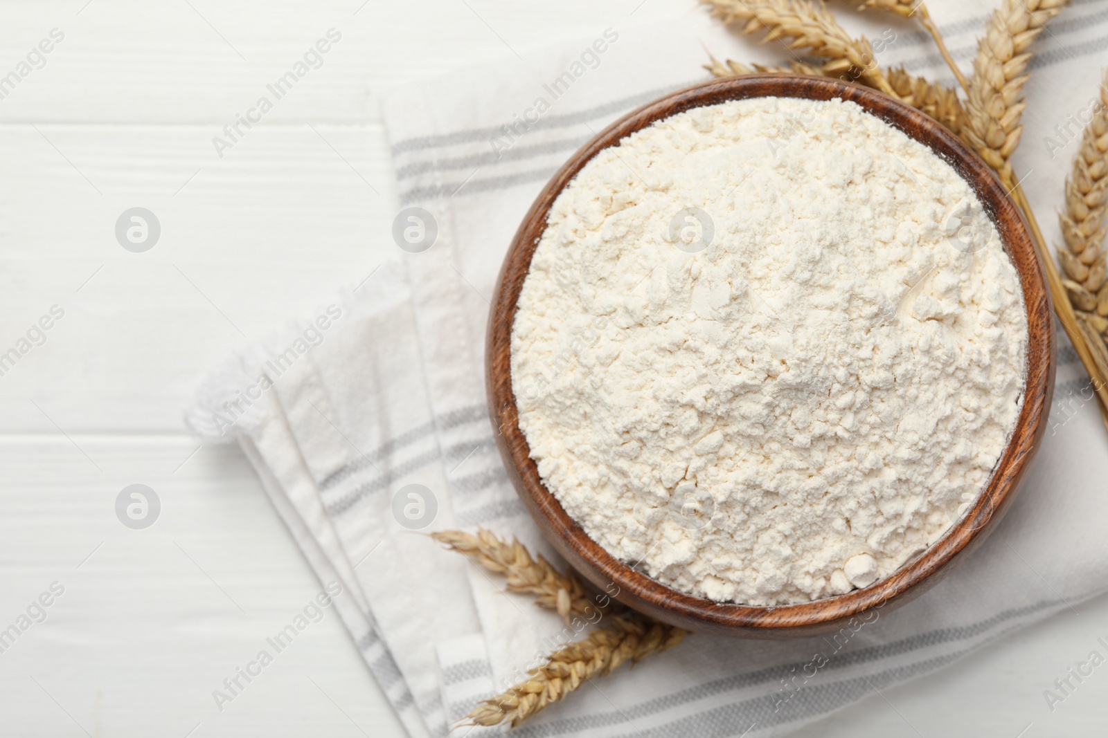 Photo of Bowl of organic wheat flour on white wooden table, flat lay. Space for text