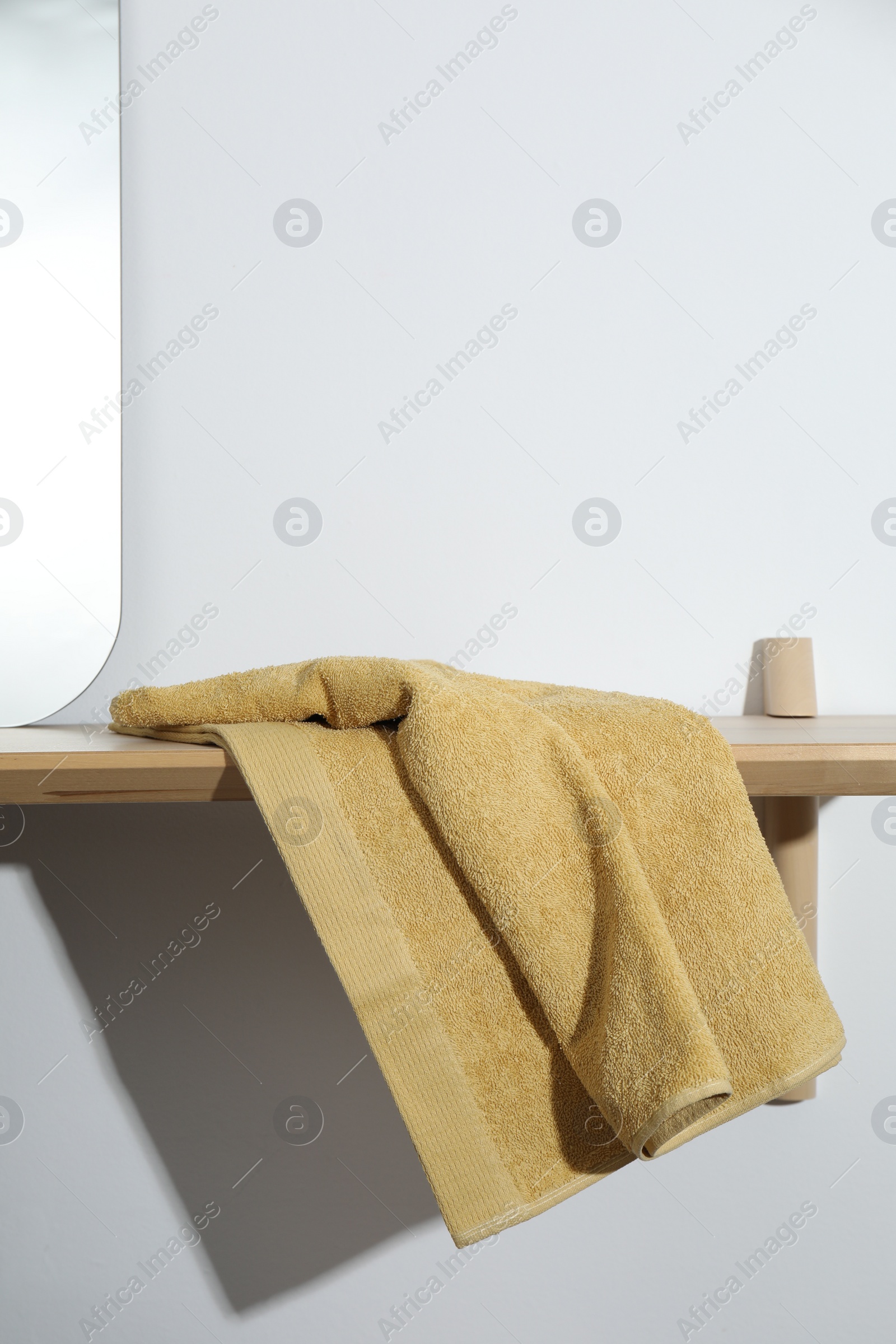 Photo of Yellow terry towel on wooden shelf near white wall