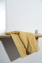 Yellow terry towel on wooden shelf near white wall