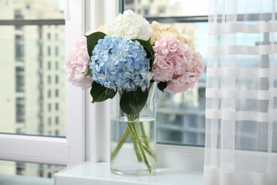 Photo of Beautiful hydrangea flowers in vase on windowsill indoors