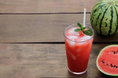 Photo of Glass of delicious watermelon drink with mint, ice cubes and fresh fruits on wooden table, space for text