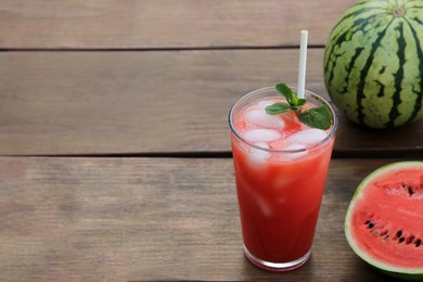 Glass of delicious watermelon drink with mint, ice cubes and fresh fruits on wooden table, space for text