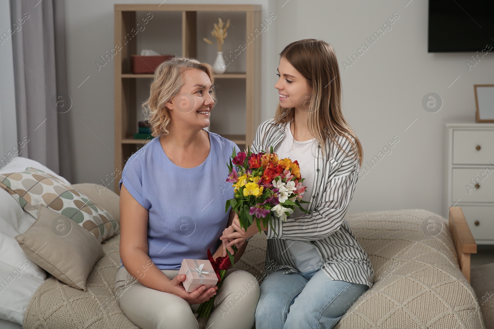 Photo of Young daughter congratulating her mom with flowers at home. Happy Mother's Day