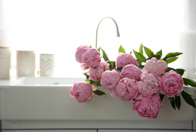 Photo of Bouquet of beautiful pink peonies in kitchen sink