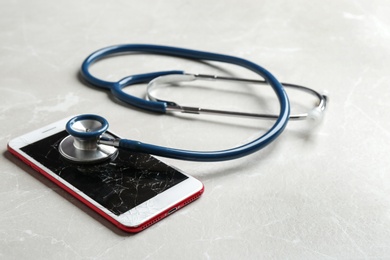 Photo of Modern smartphone with broken display and stethoscope on table. Device repair service