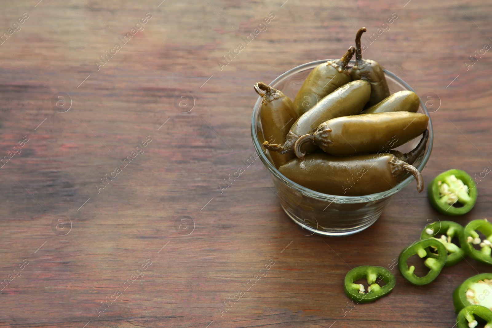 Photo of Fresh and pickled green jalapeno peppers on wooden table. Space for text