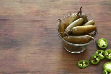 Photo of Fresh and pickled green jalapeno peppers on wooden table. Space for text