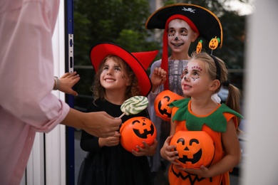 Photo of Cute little kids wearing Halloween costumes and trick-or-treating at doorway