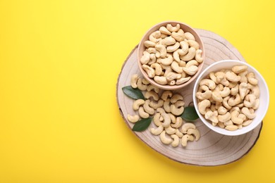 Photo of Tasty cashew nuts and green leaves on yellow background, top view. Space for text