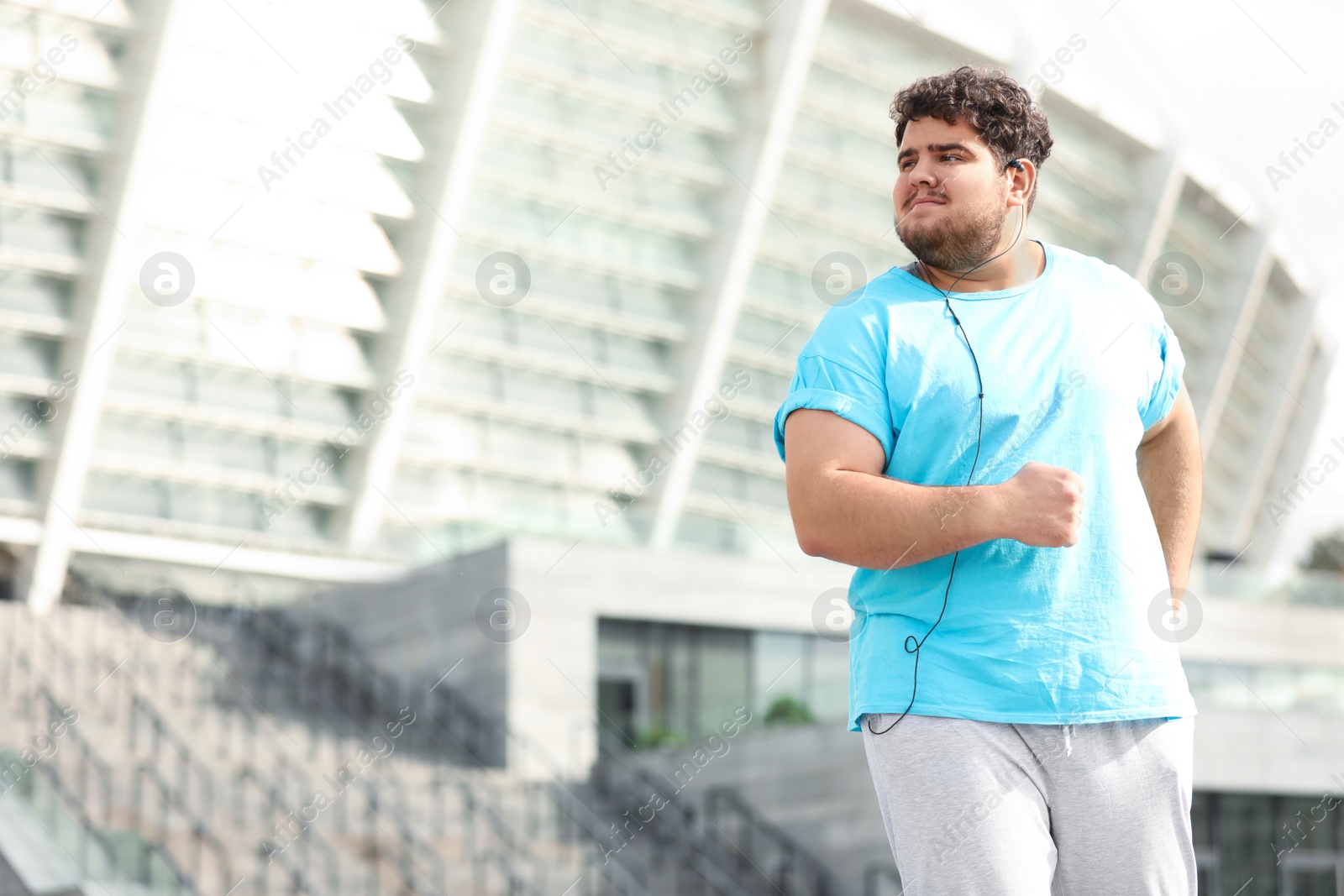 Photo of Young overweight man wearing earphones training outdoors