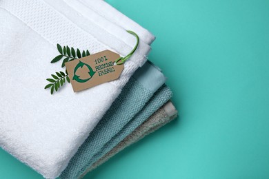 Photo of Stacked towels with recycling label and plant on turquoise background, top view. Space for text