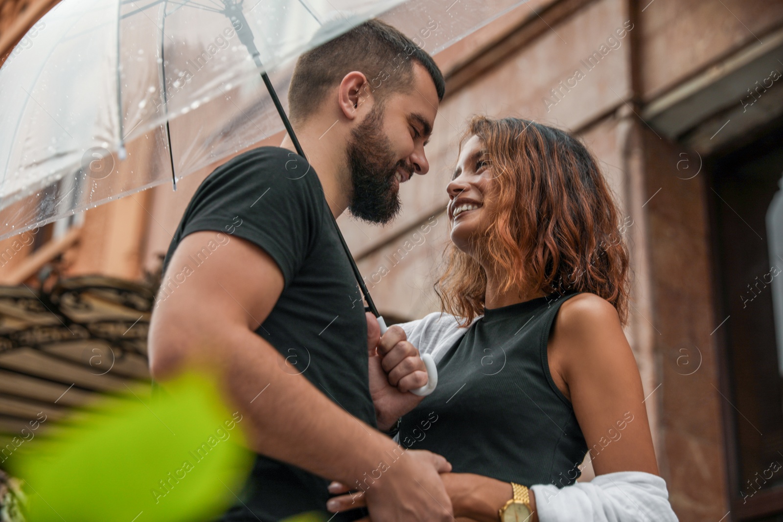 Photo of Young couple with umbrella enjoying time together under rain on city street