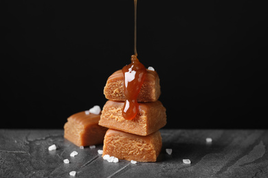 Photo of Pouring delicious salted caramel on candies against black background