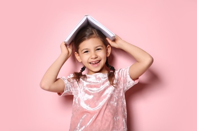 Cute little girl with book on color background