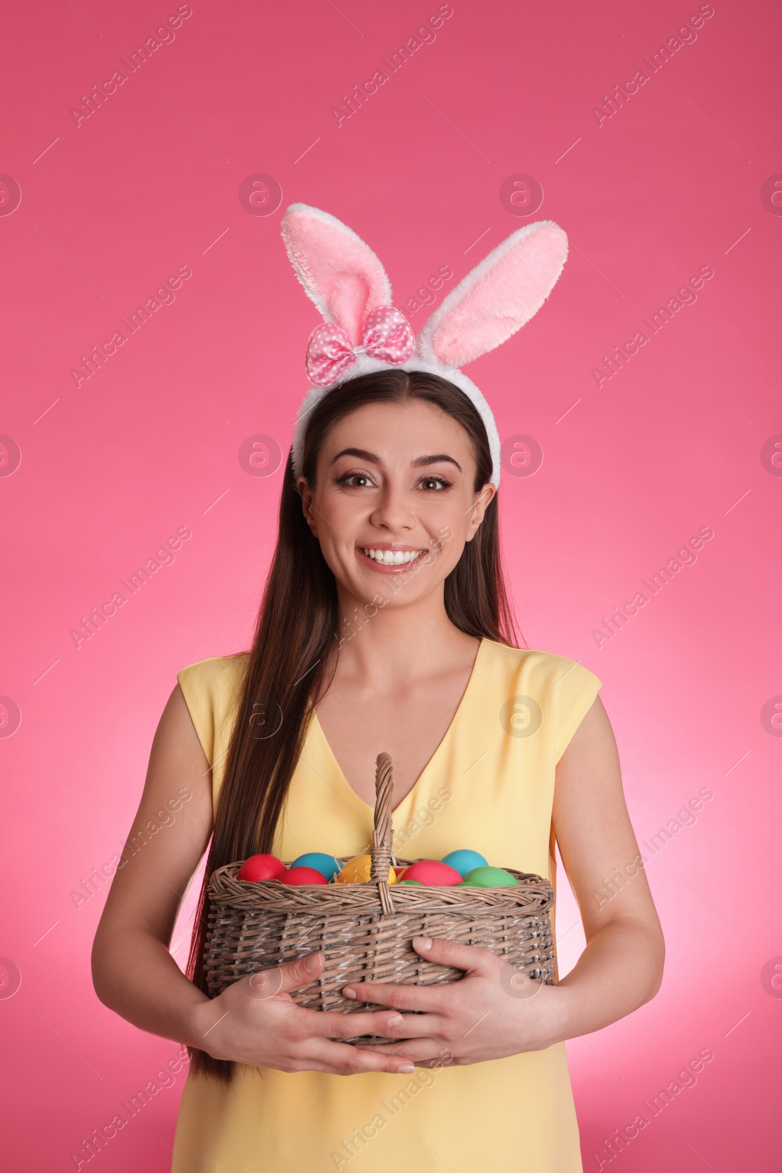 Photo of Beautiful woman in bunny ears headband with Easter eggs on color background