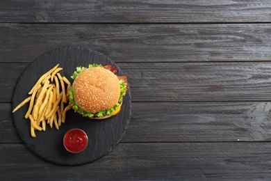 Photo of Slate plate with tasty burger and french fries on wooden background, top view. Space for text