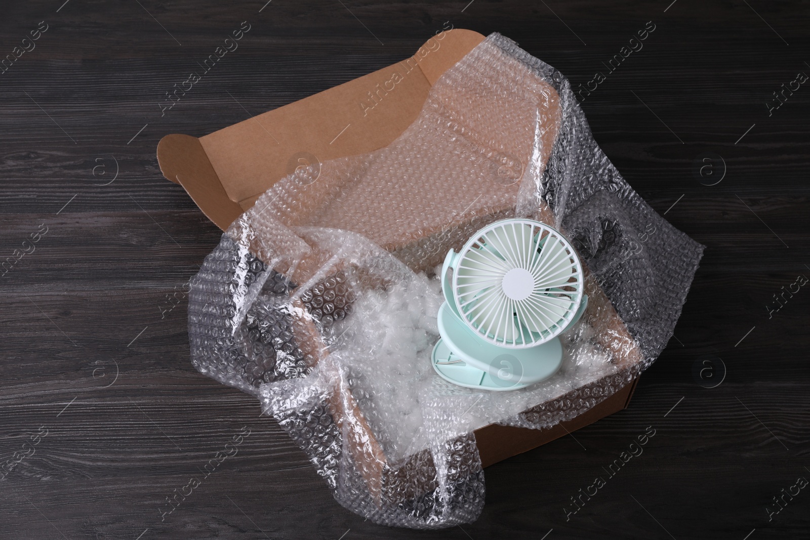 Photo of Small fan with bubble wrap and packaging foam in cardboard box on dark wooden table