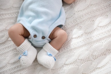 Photo of Cute newborn baby in crocheted booties on white knitted plaid, top view. Space for text