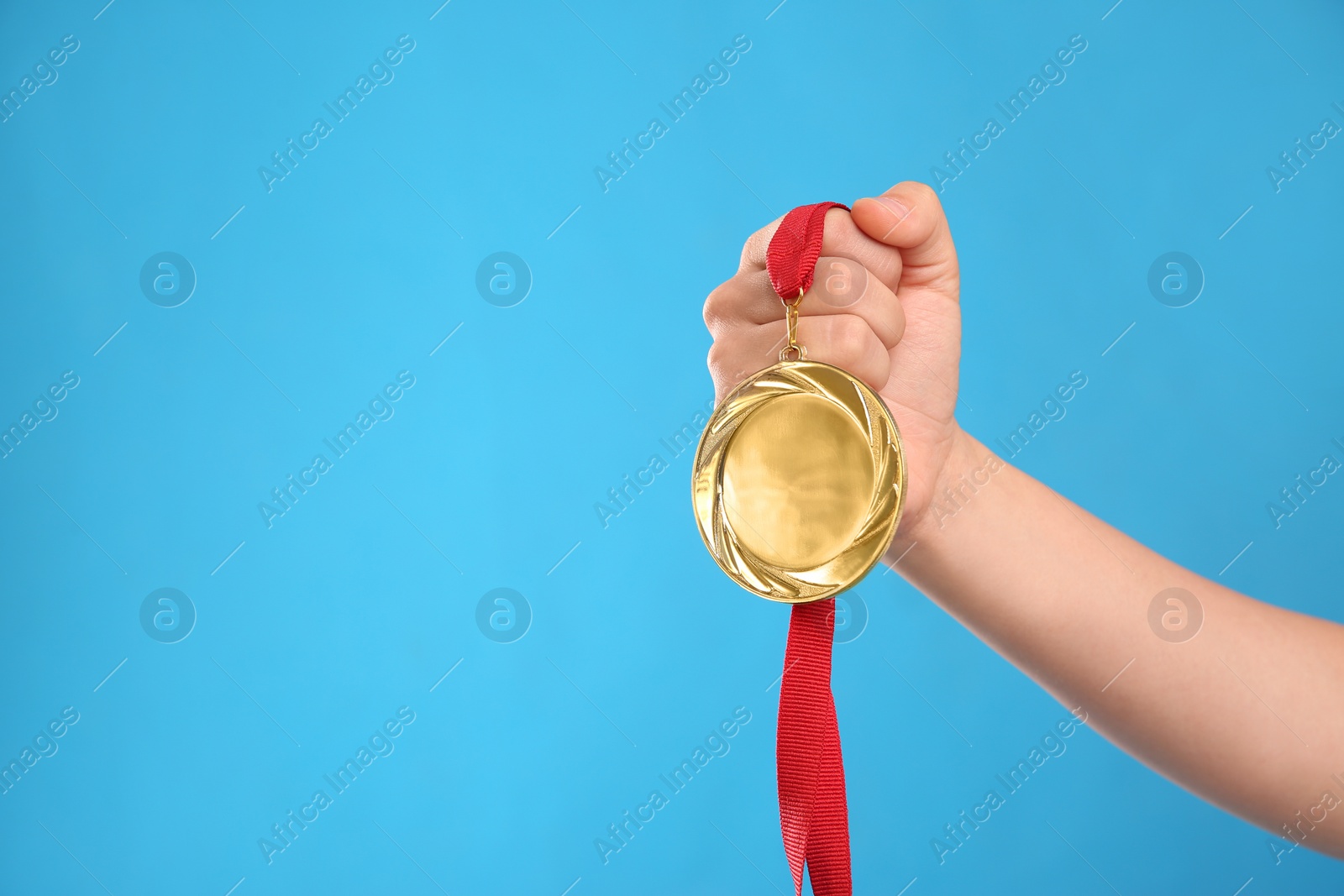 Photo of Woman holding gold medal on light blue background, closeup. Space for text