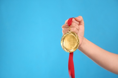 Photo of Woman holding gold medal on light blue background, closeup. Space for text