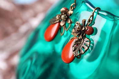 Photo of Beautiful pair of metal earrings with red jasper gemstones on glass stand, closeup