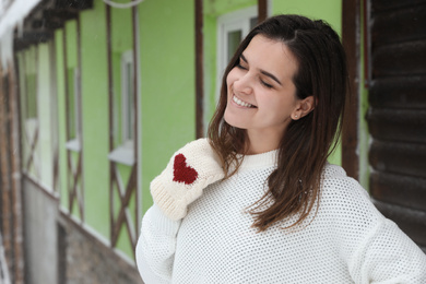Photo of Young woman wearing warm sweater and mittens  outdoors on snowy day. Winter season