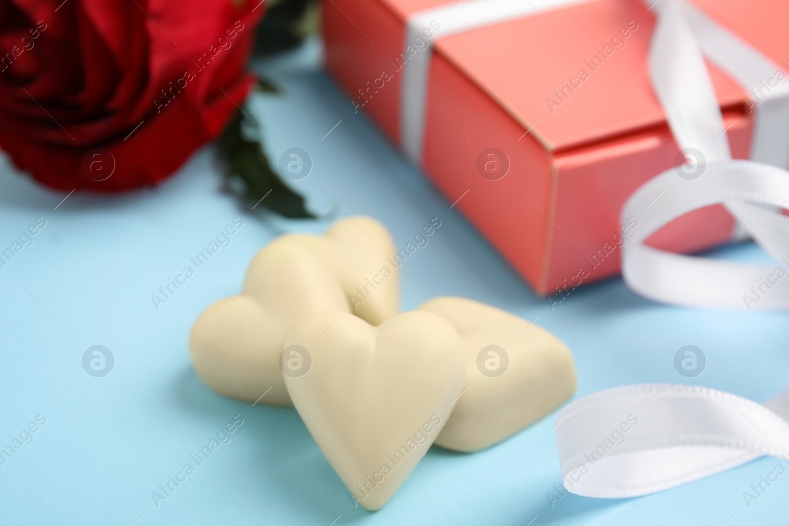 Photo of Tasty heart shaped chocolate candies on light blue background, closeup. Valentine's day celebration