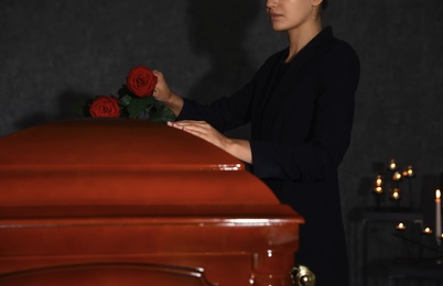 Young woman putting red rose onto casket lid in funeral home, closeup