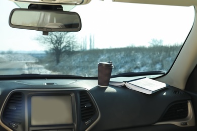 Photo of Paper cup with hot beverage and book on dashboard in car. Cozy atmosphere