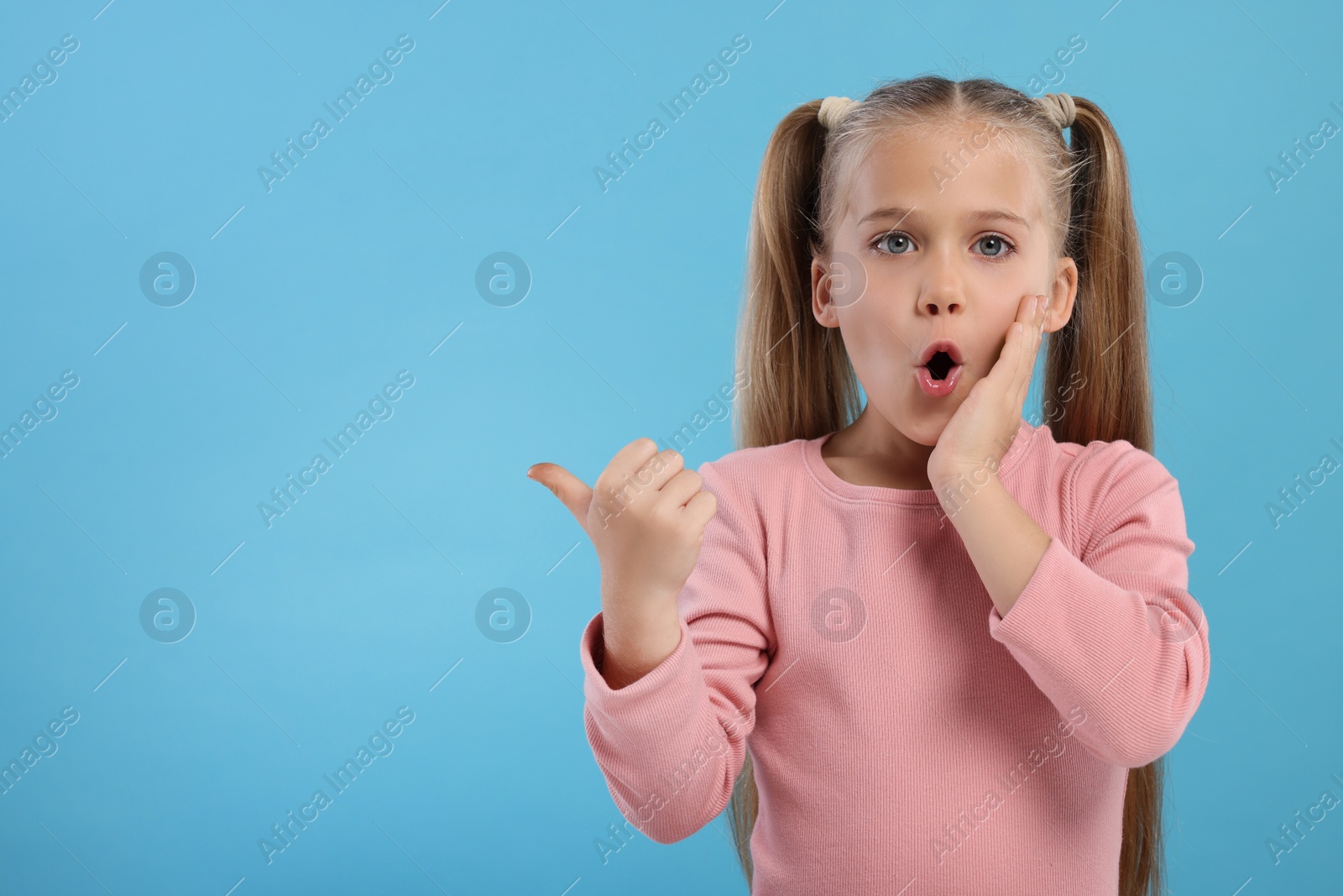 Photo of Special promotion. Emotional little girl pointing at something on light blue background. Space for text