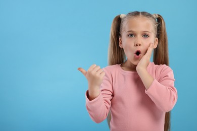 Special promotion. Emotional little girl pointing at something on light blue background. Space for text