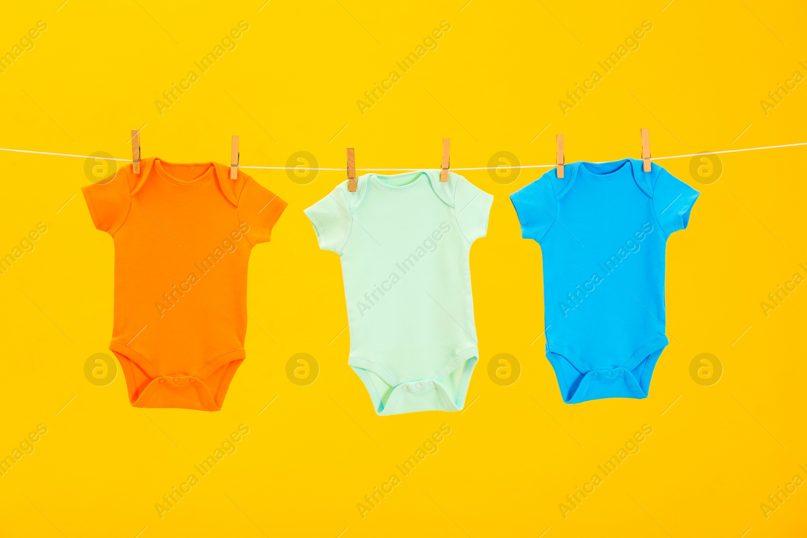 Photo of Baby onesies hanging on clothes line against yellow background