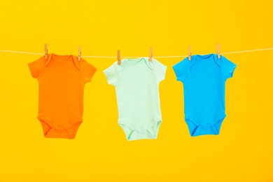 Photo of Baby onesies hanging on clothes line against yellow background