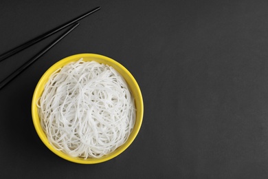 Cooked rice noodles and chopsticks on black background, flat lay. Space for text