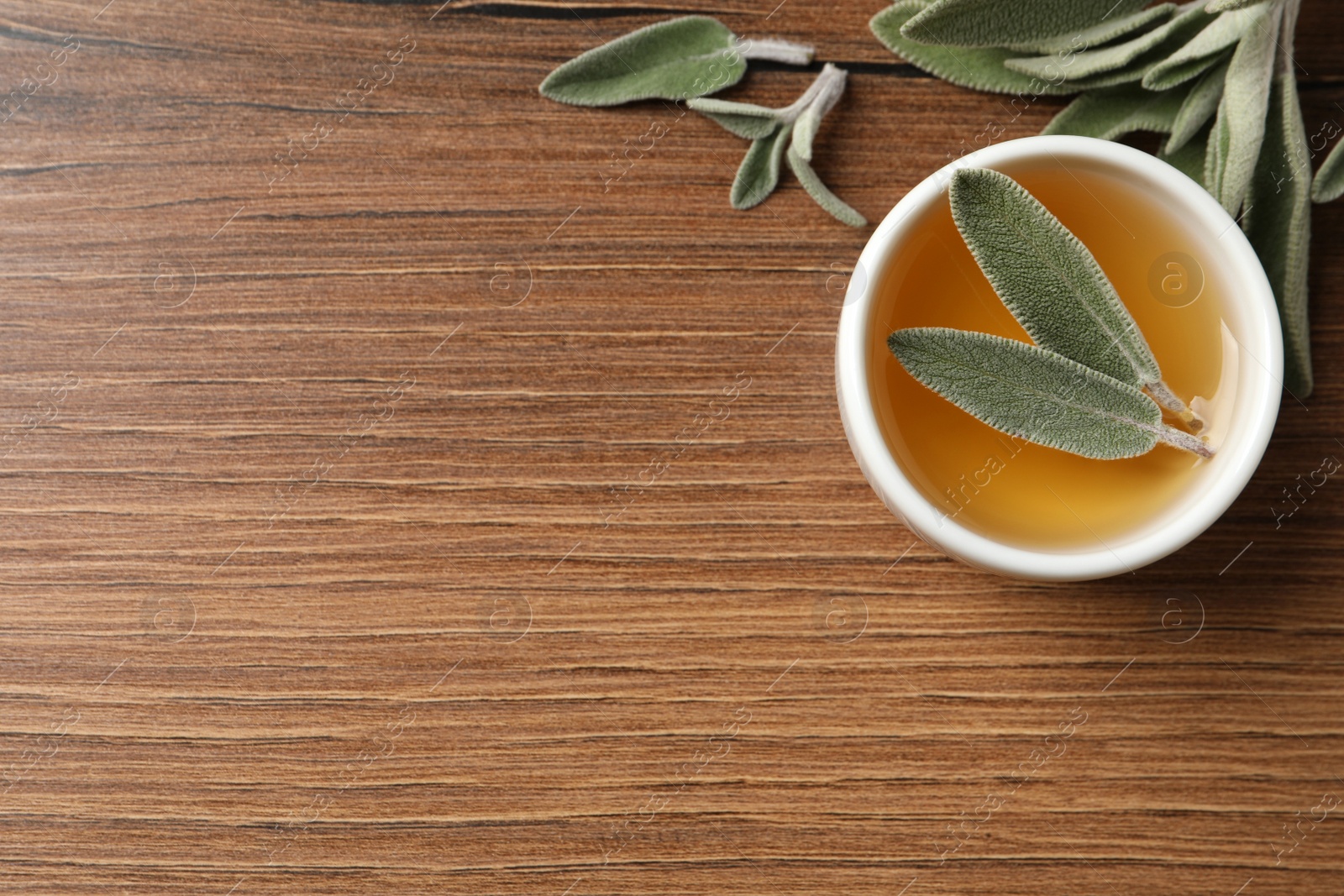 Photo of Bowl of essential sage oil and leaves on wooden table, flat lay. Space for text