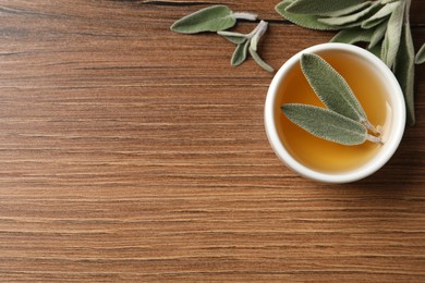 Photo of Bowl of essential sage oil and leaves on wooden table, flat lay. Space for text