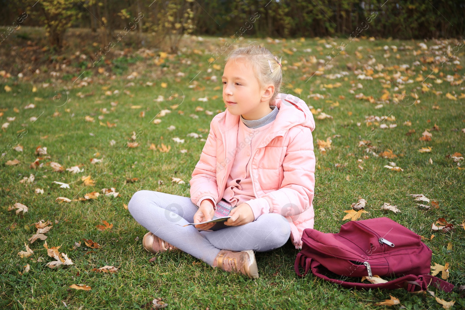 Photo of Cute little girl with copybook and backpack on green grass outdoors