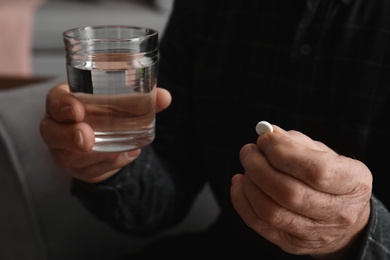 Senior man holding pill and glass of water, closeup