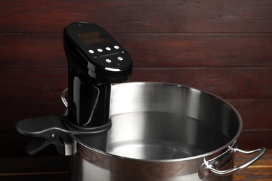 Photo of Thermal immersion circulator in pot on wooden table. Sous vide cooker