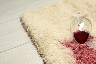 Photo of Overturned glass and spilled red wine on beige carpet, closeup. Space for text