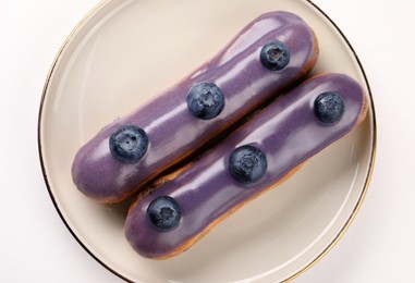 Photo of Delicious eclairs decorated with blueberries on white background, top view