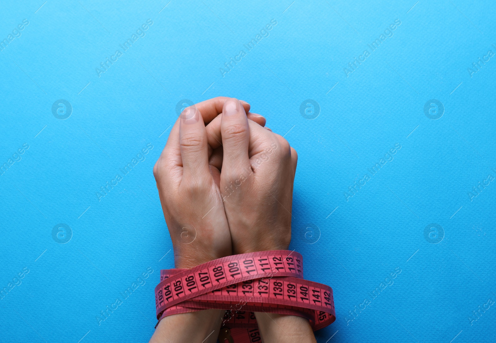 Photo of Woman tied with measuring tape on light blue background, top view. Diet concept