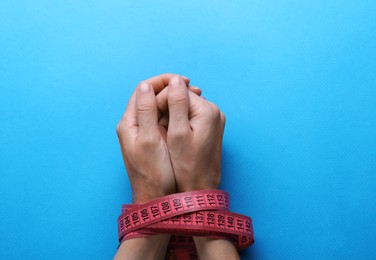 Woman tied with measuring tape on light blue background, top view. Diet concept